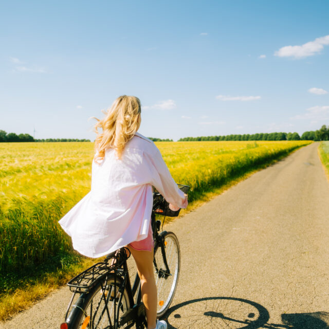 lyshåret kvinde på cykel ved en mark på en sommerdag